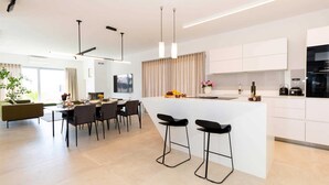 Una cocina moderna con una isla central, taburetes de bar, iluminación colgante y un comedor con sillas y una mesa.