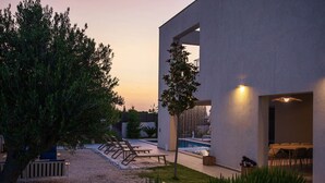 Un espacio exterior moderno con piscina, sillones de descanso y zona de comedor.