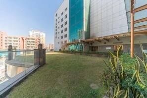 A modern building with a rooftop pool, a grassy area, and a view of other buildings.
