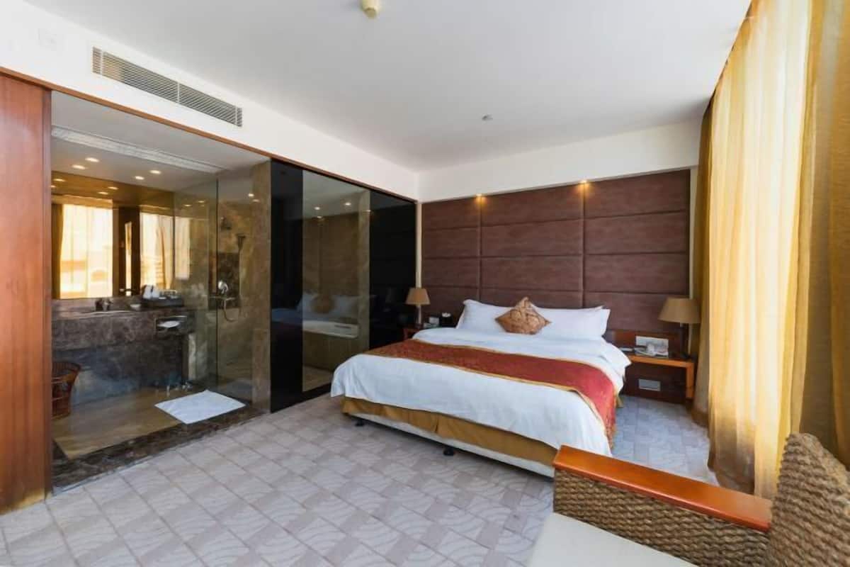 Une chambre d’hôtel comprenant un lit, une table de chevet, une douche en verre et donnant sur une piscine.
