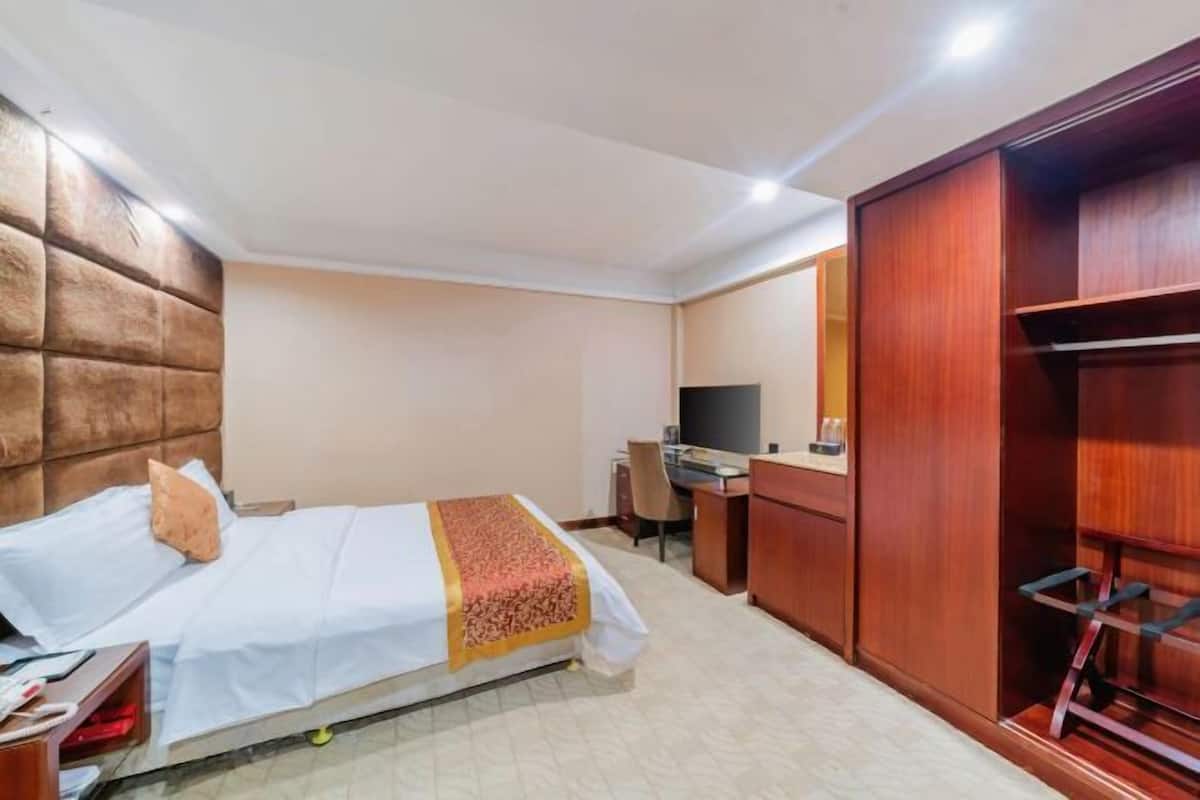 Une chambre d’hôtel comprenant un lit, un bureau, une télévision, une armoire et un petit coin salon.