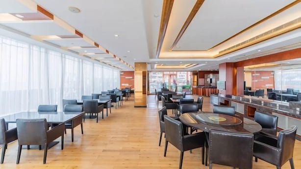 Un hall d’hôtel spacieux, doté de plusieurs espaces salon, d’un bar central et de grandes fenêtres laissant entrer la lumière naturelle.
