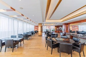 A spacious hotel lobby with multiple seating areas, a central bar, and large windows providing natural light.
