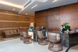 A reception area with a reception desk, wicker chairs, a sofa, and a large plant.