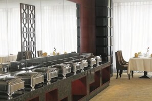 A buffet setup with multiple serving stations, a large mirror, and a dining area with a table and chairs. - Huangjiang Holiday Hotel (Dongguan)