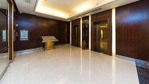 Un hall d’hôtel avec un sol en marbre, des boiseries, un comptoir d’accueil et un ascenseur.