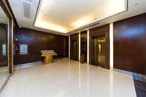 Un vestíbulo de hotel con suelo de mármol, paneles de madera, una recepción y un ascensor.