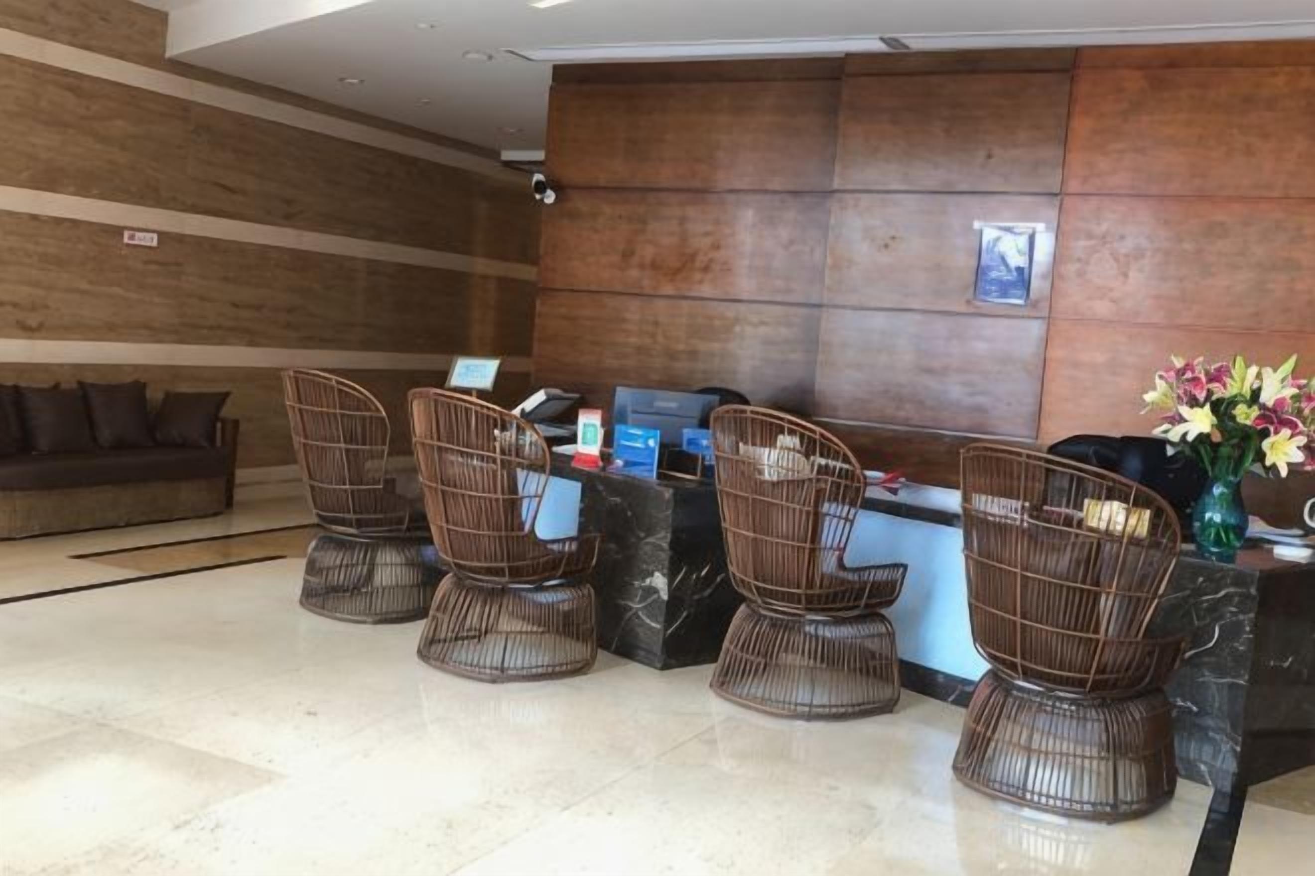 Un área de recepción con mostrador, cuatro sillas de mimbre, un sofá y un jarrón con flores.