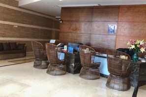 Een receptiegedeelte met een receptiebalie, vier rieten stoelen, een bank en een bloemenvaas.