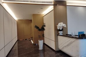 A hotel reception area with a marble reception desk, a potted plant, and a wall-mounted vase with white flowers. - Huangjiang Holiday Hotel (Dongguan)