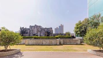 Un área ajardinada con una formación rocosa, un sendero pavimentado y un edificio al fondo.