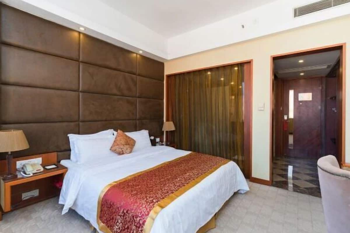 Une chambre d’hôtel avec un grand lit, une tête de lit, une table de chevet avec une lampe et une porte donnant sur une autre pièce.
