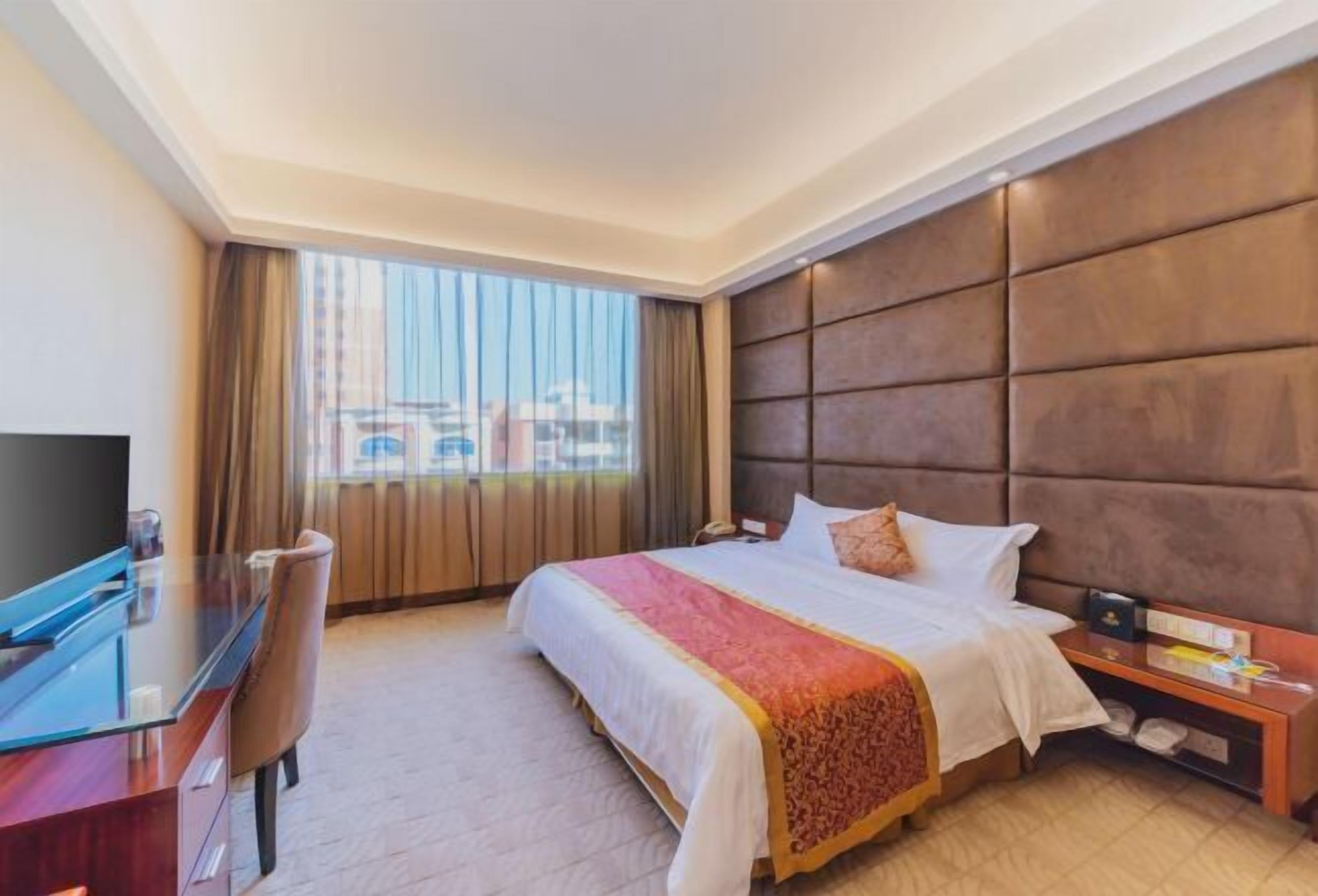 A hotel room with a large bed, a desk with a chair, a television, and a nightstand with a phone.