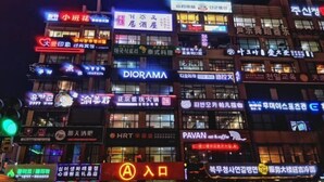 A building with multiple illuminated signs, including brands like Diorama and HRT. - Apple Apartment (Yanji)
