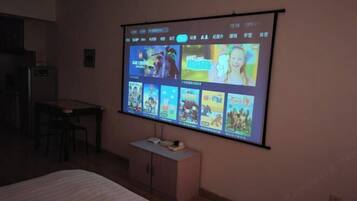 A room with a bed, a desk, a chair, and a wall-mounted projector screen displaying various images.