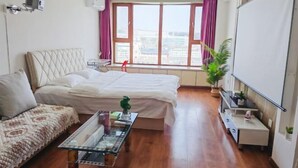 A hotel room with a bed, a sofa, a small table, a TV, a window with curtains, and a potted plant. - Apple Apartment (Yanji)