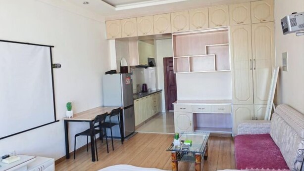 A compact hotel room with a bed, a desk, a chair, a kitchenette, and a seating area with a sofa. - Apple Apartment (Yanji)