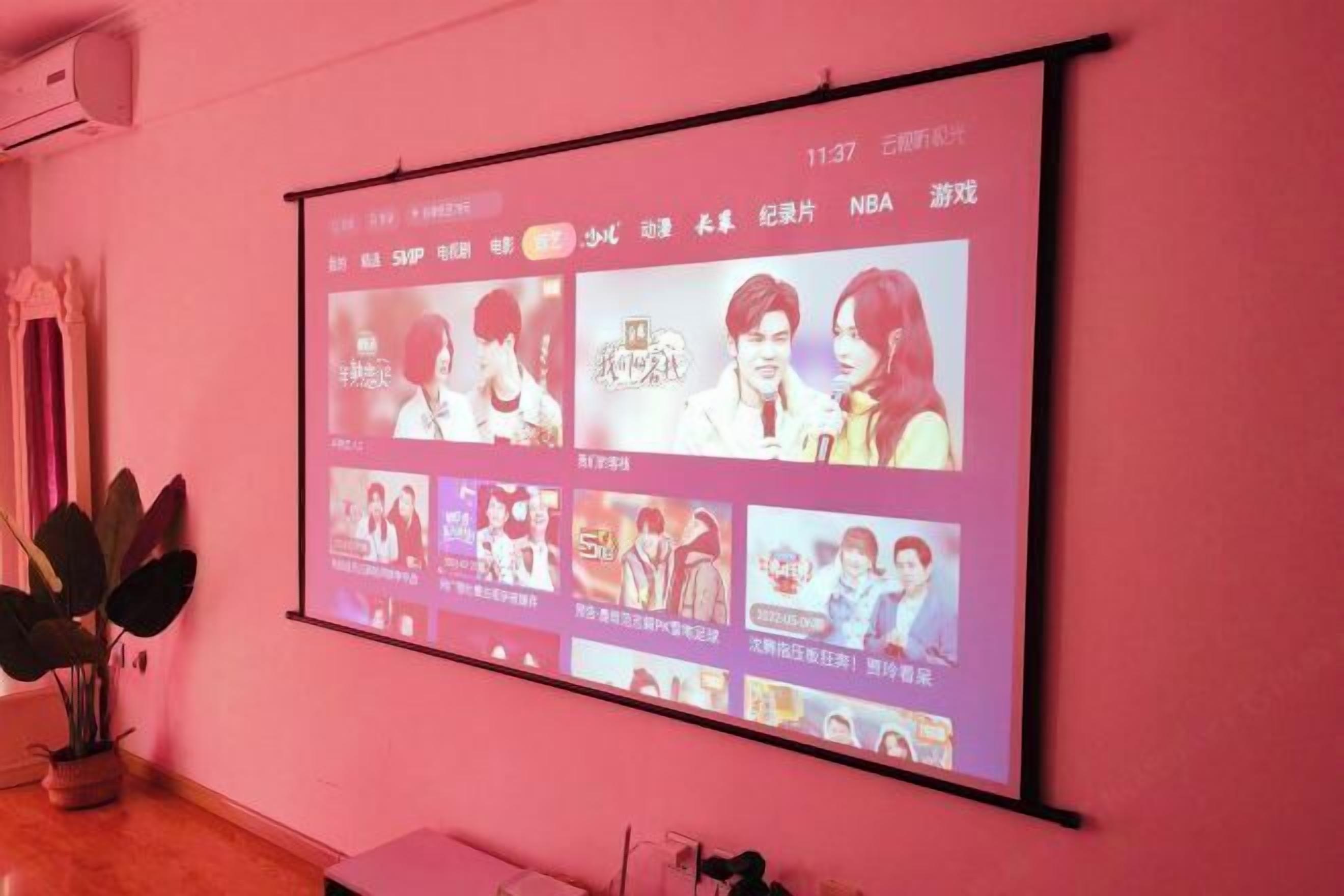A projection screen displaying various entertainment content on a pink wall.