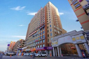 A multi-story hotel with a prominent entrance, several ground-level shops, and a clear sky.