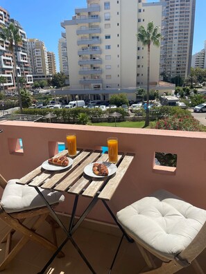 An outdoor dining area with a table set for two, overlooking a parking lot and a cityscape with high-rise buildings. - Charming duplex apartment with a terrace and a view of the pool, 200 m from the beach (Portimão)