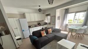 Un espacio habitable compacto con kitchenette, un sofá con cojines de colores, una zona de comedor con mesa y sillas, y un ventanal que ofrece vistas al exterior.