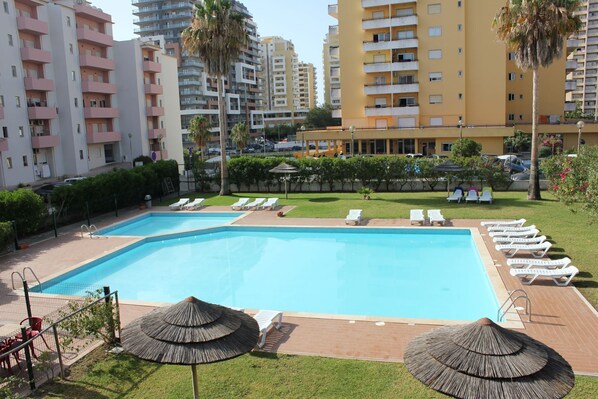 A swimming pool with lounge chairs and umbrellas, surrounded by apartment buildings. - Charming duplex apartment with a terrace and a view of the pool, 200 m from the beach (Portimão)
