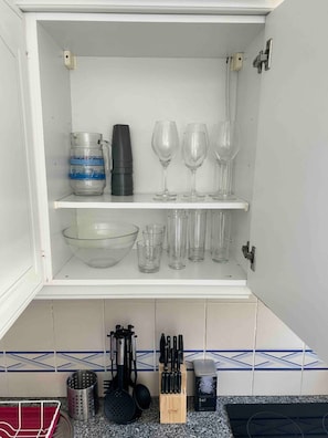 A kitchen cabinet with shelves holding various glassware and kitchen utensils. - Charming duplex with a terrace and a view of the pool, 200 m from the beach (Portimão)