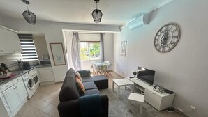 Un espacio habitable compacto con sofá, televisor, mesa de comedor y zona de cocina.