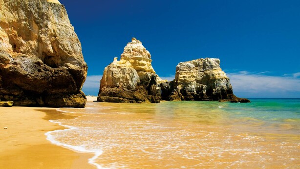 Una playa con aguas turquesas cristalinas, una orilla arenosa y grandes formaciones rocosas.