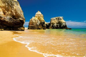 A beach with clear turquoise water, sandy shore, and large rock formations. - Charming duplex apartment with a terrace and a view of the pool, 200 m from the beach (Portimão)