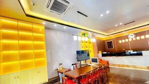 Un moderno vestíbulo de hotel con un mostrador de recepción de madera, un televisor y una zona de estar con sillas rojas.