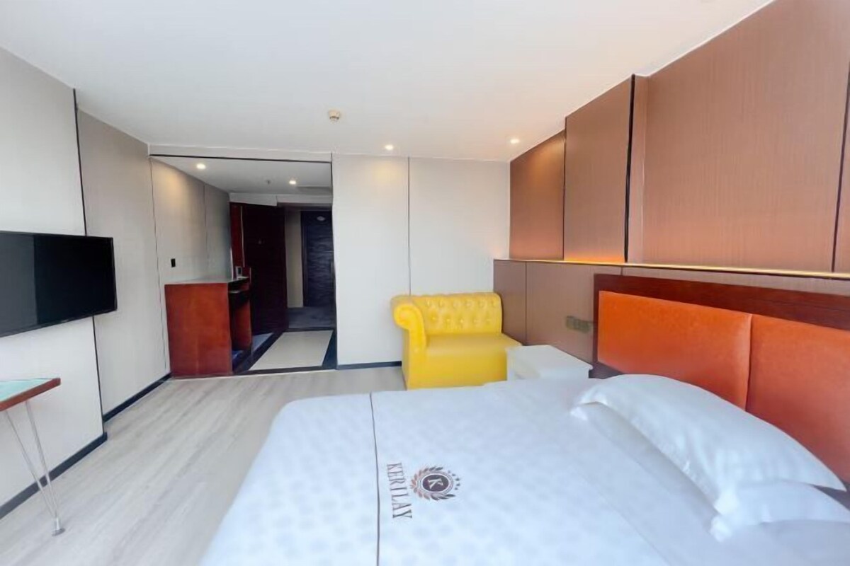 A hotel room with a bed, a TV, a yellow armchair, and a wooden headboard.