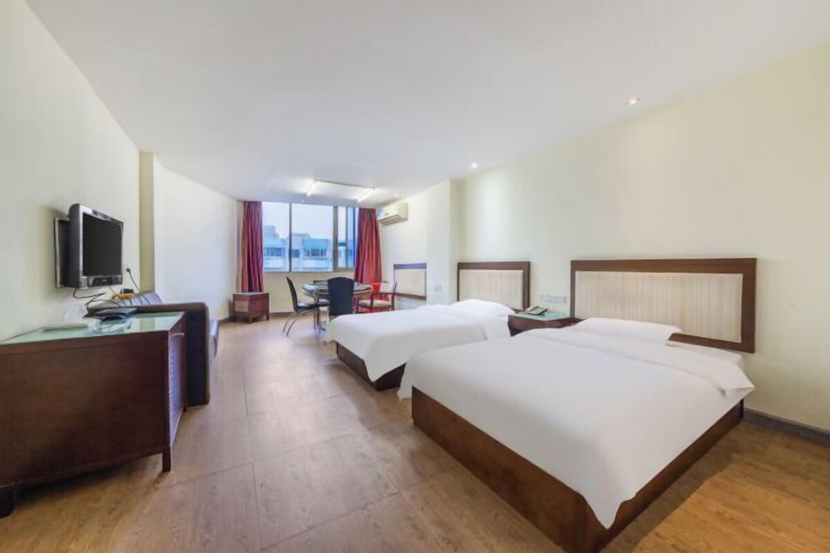 A hotel room with two beds, a desk with a computer, a television, and a window with curtains.