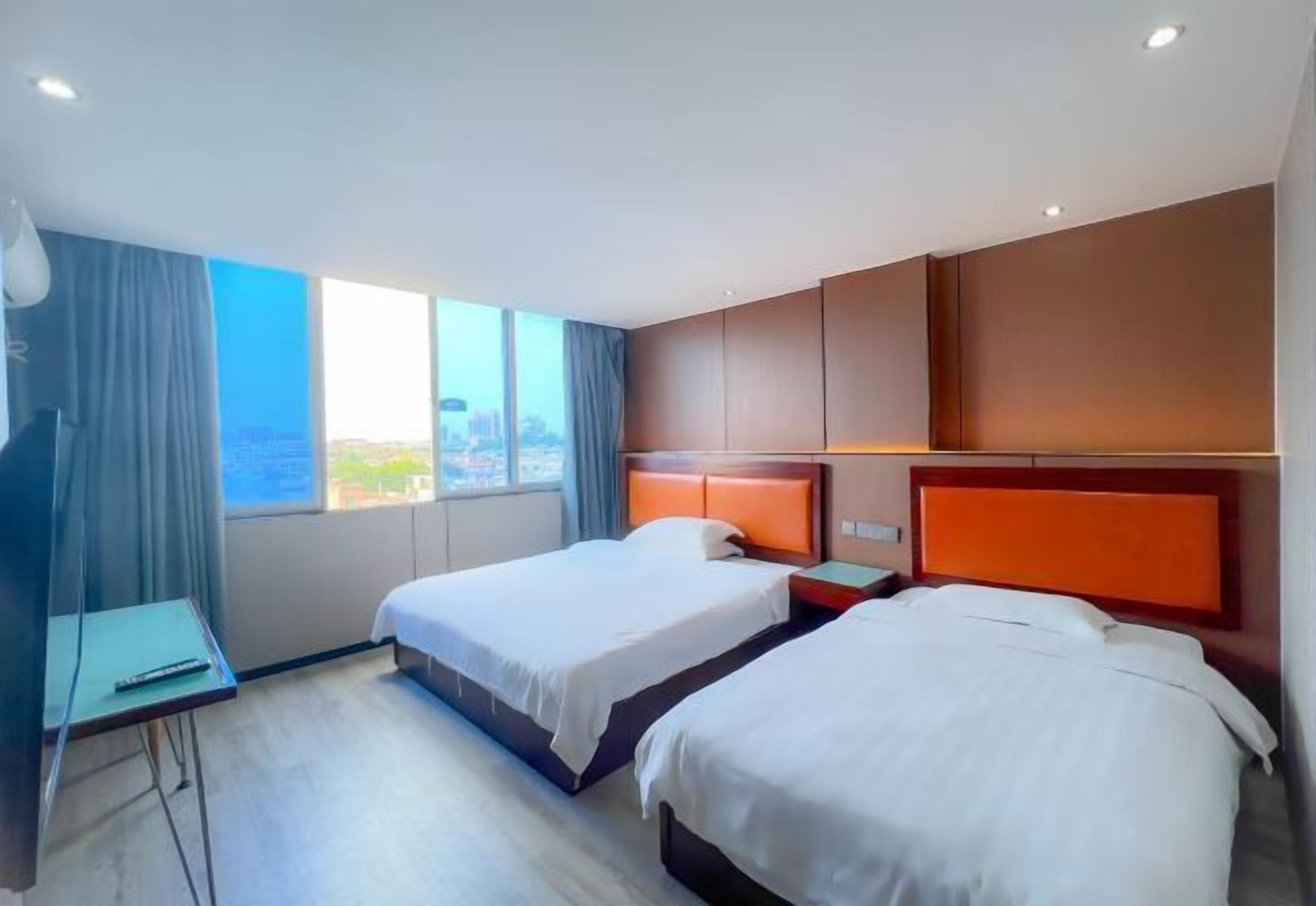 Une chambre d’hôtel avec deux lits, un bureau et une grande fenêtre donnant sur la ville.