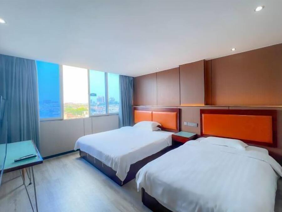 Habitación de hotel con dos camas, un escritorio y un ventanal grande con vista a la ciudad.