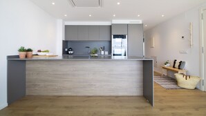 A modern kitchen with grey cabinets, a wooden countertop, and a built-in oven. There is a small seating area with a bench and a basket. - Apt. 1st line of the sea, spectacular views 6 pax, wifi and air conditioning. Vivalidays Apartour. (Calella)