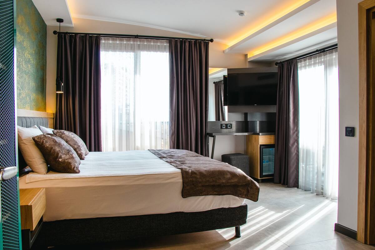 A modern hotel room with a large bed, a flat-screen TV, and a minibar.