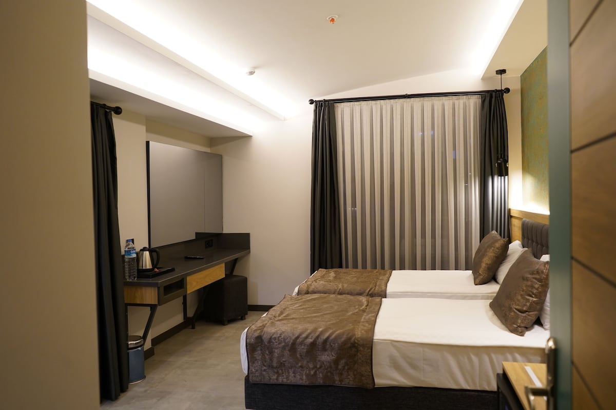 Habitación de hotel con dos camas, un escritorio, una silla, un espejo y una ventana con cortinas.