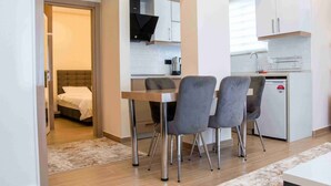 Habitació d'hotel senzilla amb llit, una cuineta petita i zona de menjador amb taula i cadires.