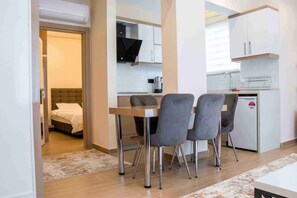 Habitación de hotel compacta con cama, kitchenette pequeña y zona de comedor con mesa y sillas.