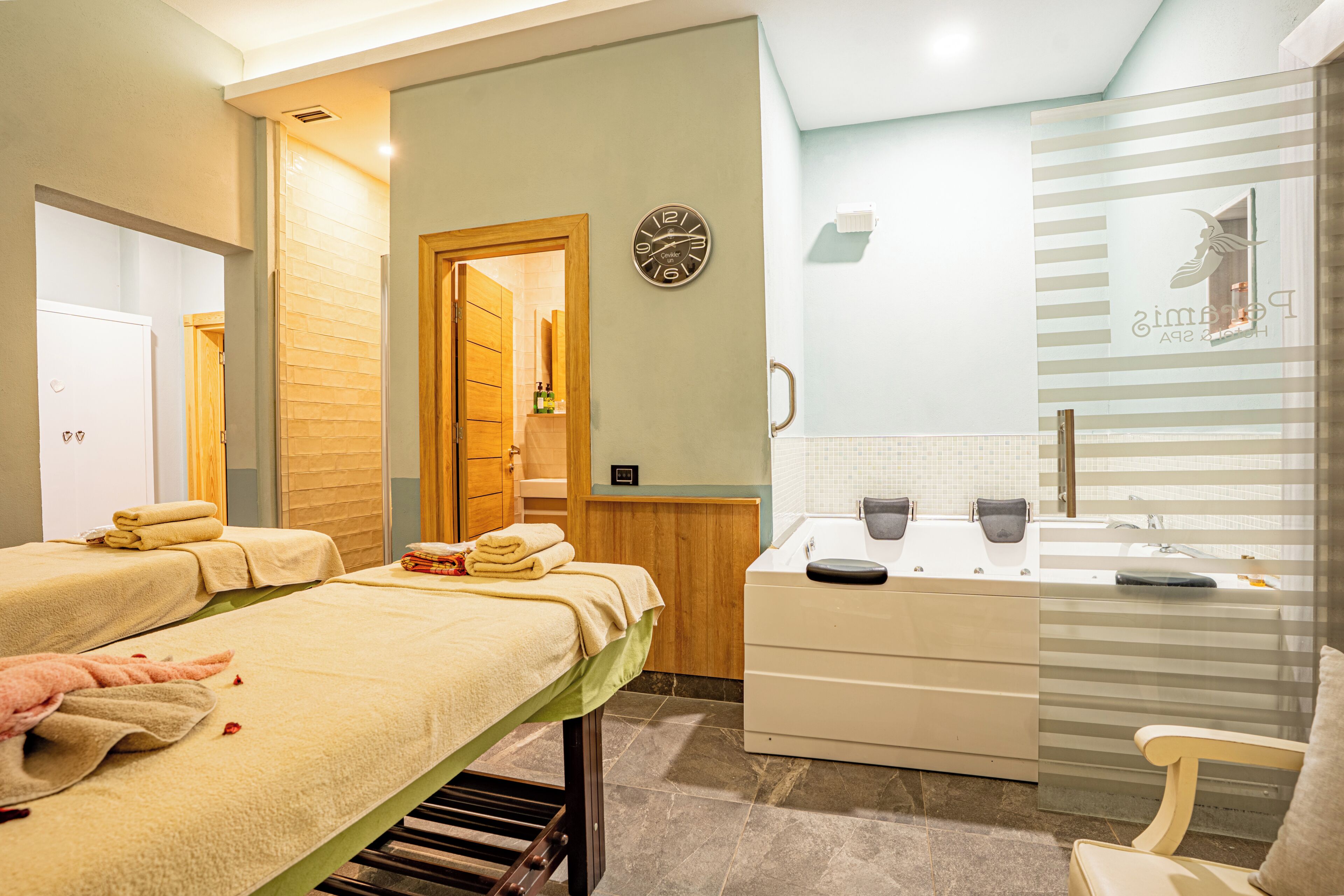 A hotel room with a massage table, a small desk with a chair, a mirror, and a clock on the wall.
