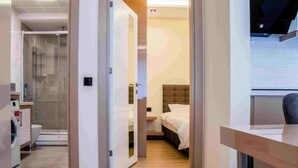 Habitació d'hotel moderna amb un envàs de dutxa de vidre, un llit amb capçal tapissat i un terra de fusta.