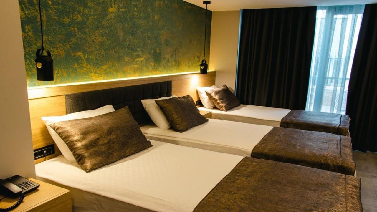 Habitación de hotel con dos camas, cabecero de madera, teléfono y pared con diseño texturizado.