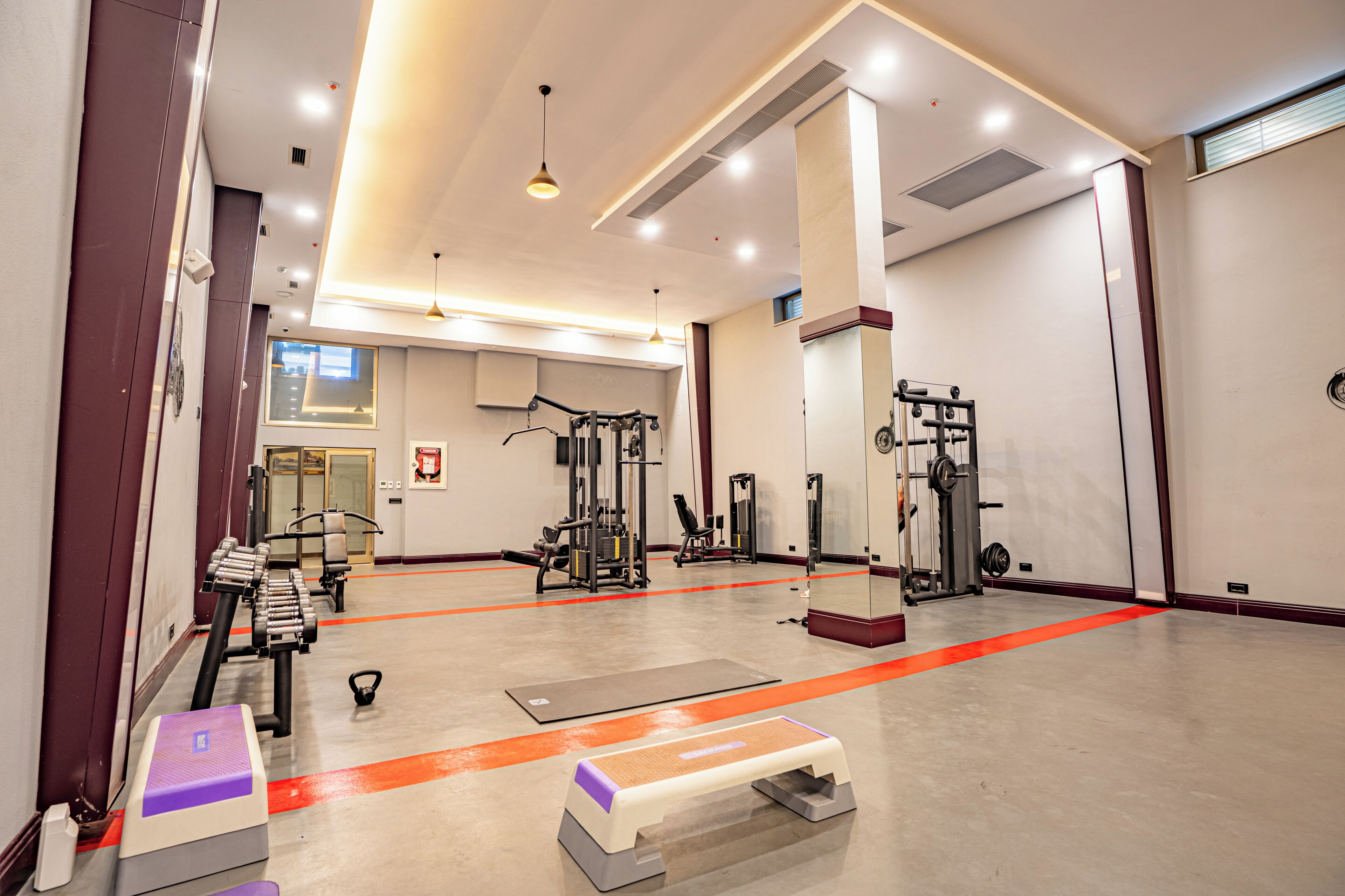 A gym with exercise equipment, a mirror, and a red line on the floor.