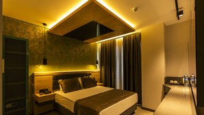 Quarto de hotel moderno com uma cama grande, mesas de cabeceira, uma escrivaninha e um candeeiro suspenso.