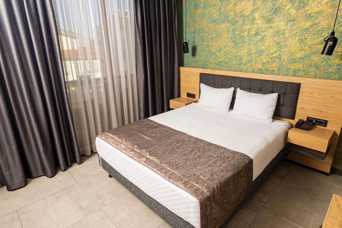 A hotel room with a bed, bedside tables, a telephone, and a lamp.