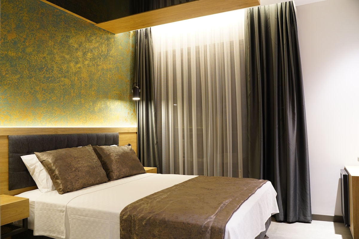 Habitación de hotel con cama, cortinas, una mesita de noche y una pared con textura.