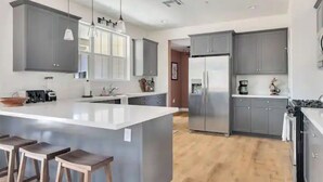 A modern kitchen with grey cabinets, a central island with stools, and a stainless steel refrigerator. - Mirasol Manor -sleeps up to 14! Minutes to Paso + SLO (Atascadero)