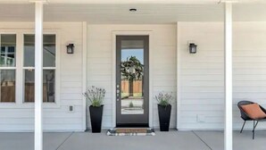 A white house with a front door, two potted plants, a chair, and a small porch area. - Mirasol Manor -sleeps up to 14! Minutes to Paso + SLO (Atascadero)