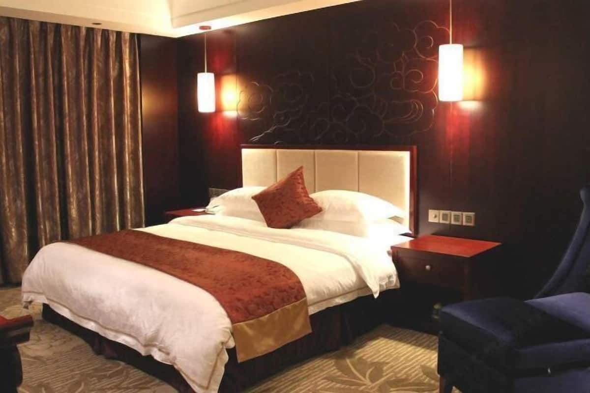 Habitación de hotel con una cama grande, dos mesitas de noche, un sillón azul y una decoración de pared.